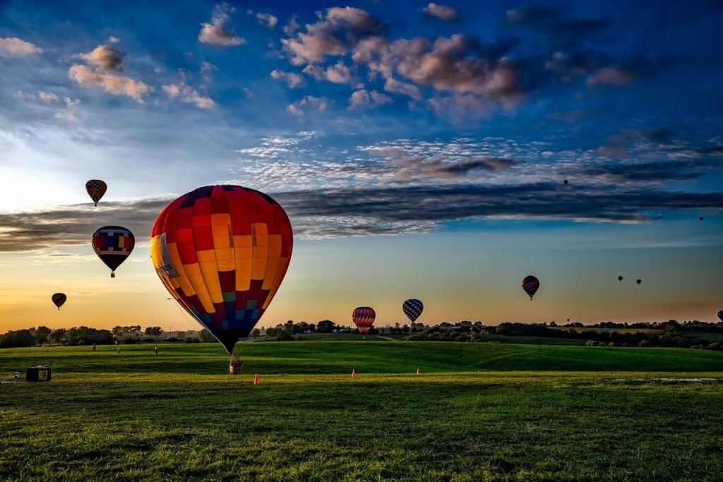 Vibrant hot air balloons take off at dawn over a rural field, showcasing a picturesque landscape.